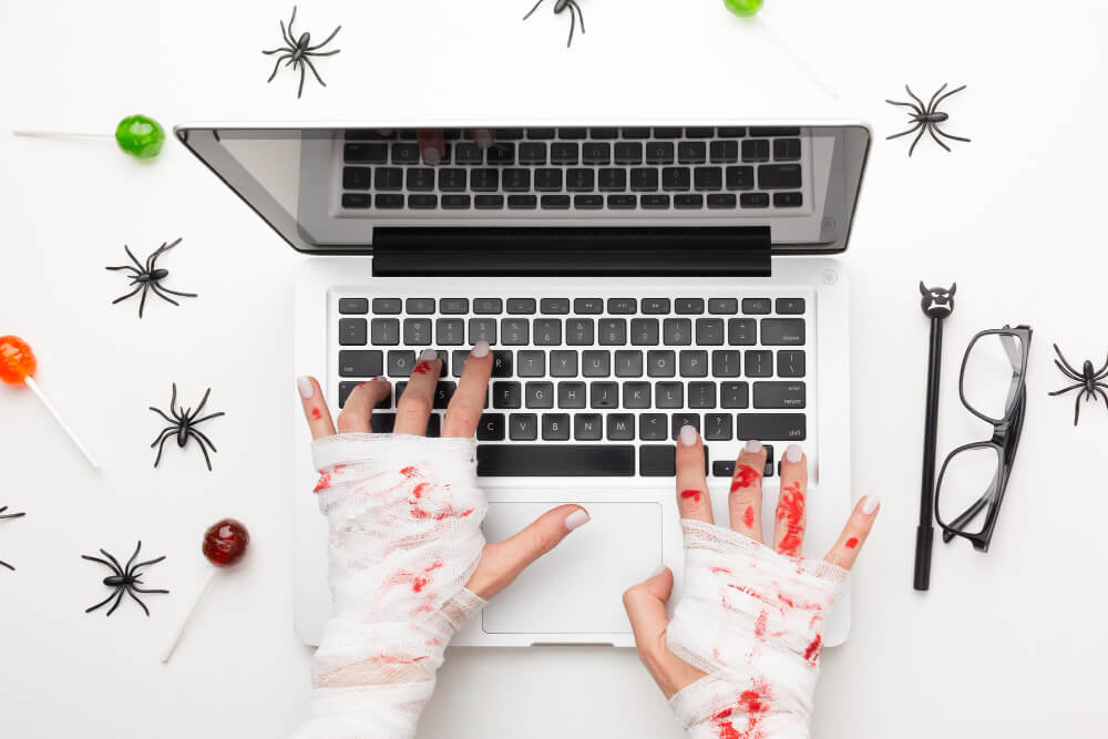 Bandaged, bloody hands using the keyboard of a laptop, with spiders surrounding the laptop