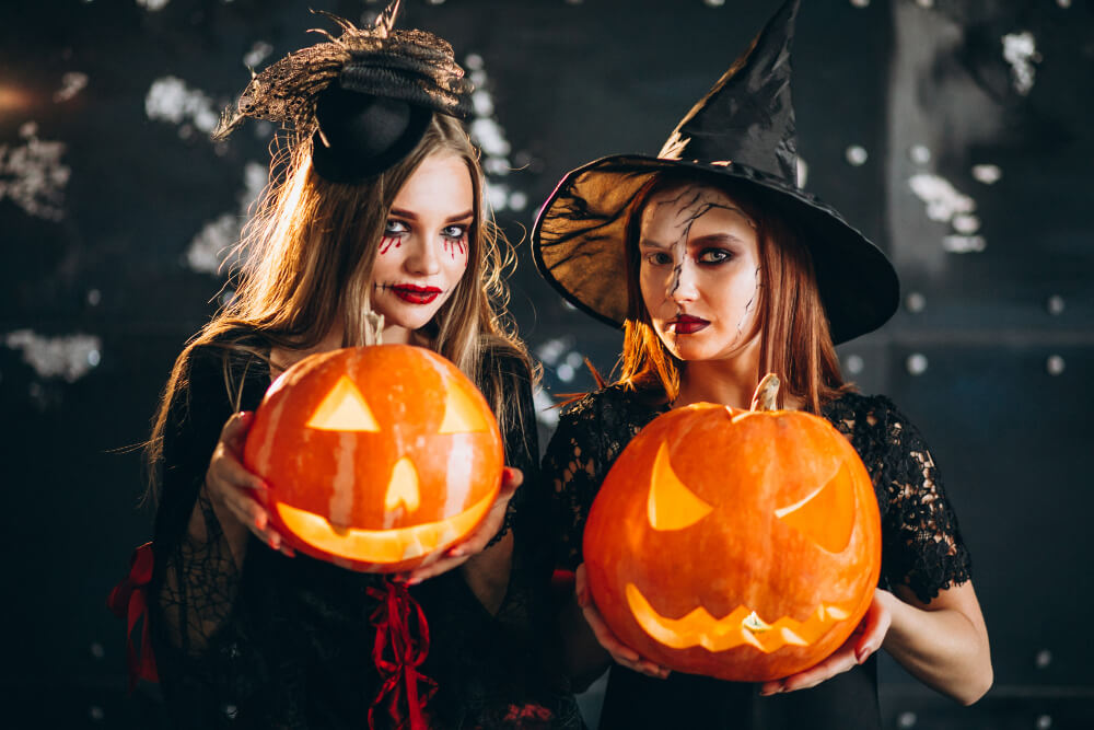 Two women dressed as witches, each holding a creepy pumpkin